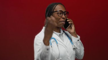Doktor, kırmızı arka planda, laboratuvar önlüğü yerine gözlük ve steteskop takan bir cep telefonuyla konuşuyor..