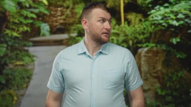 Açık mavi bir gömlek giyerken ve rahatsız bir kaş kaldırırken insan başparmağıyla orman yolunu işaret eder..