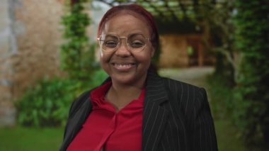 Kırmızı bluzlu gülümseyen Afrikalı Amerikalı kadın binanın girişinde kamerayı işaret ediyor; sıcak karşılama daveti.