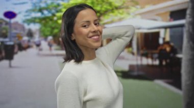 Terasta gülümseyen bir kadın hayat dolu bir sokak arkaplanı, parlak bir günde mutluluğu ve günlük yaşam tarzını somutlaştırıyor..