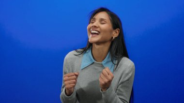 Neşeli mavi arka planda kutlama yapan bir kadın, neşeli bir ifadeyle mutluluk ve başarıyı ifade ediyor..