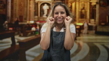 Kadın kilise binasında kot önlük giyerek ve kapalı gözlerle gülümseyerek yumruklarını sıkıyor; neşe duası..