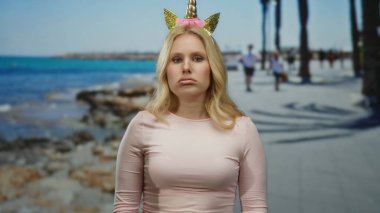 Tek boynuzlu at diademi olan kadın sahilde geziniyor. Endişeli ve endişeli görünüyor. Etrafı mavi okyanusla çevrili..