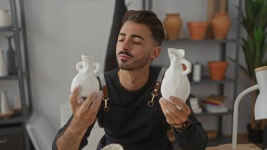 Beyaz seramik vazo tutan ve bir stüdyoda gülümseyen adam; yaratıcılık zanaatkarlığı ilham tutkusu.