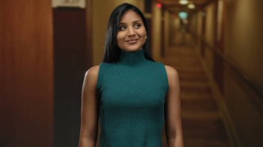 Otel koridorunda gülümseyen, deniz mavisi elbiseli, kendine güveni ve sıcaklığı olan bir kadın, modern zarafeti huzurlu bir ortamda yakalıyor..