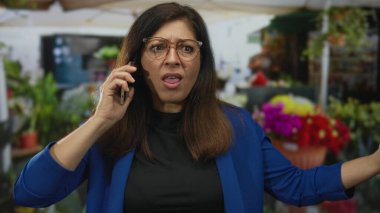 Orta yaşlı gözlüklü İspanyol kadın akıllı telefonu kulağına tutuyor ve sokakta el hareketini yükseltiyor..