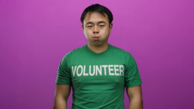 Yeşil gönüllü gömlekli genç adam neşeli pembe arka plana karşı komik bir yüz ifadesi sergiliyor.