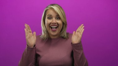 Genç sarışın kadın elleri ile gözlerini kapar ve mor bir stüdyoda gülümsemek için ellerini indirir..