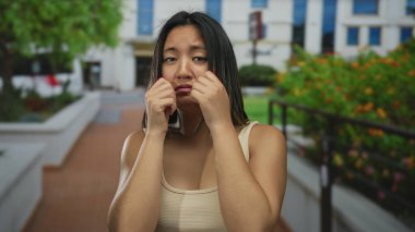 Açık havada genç bir kadın, şehir manzarası ve yeşilliklerle çevrili şehir ortamında düşünceli bir ifade, yoğun şehir yaşamının ortasında duygularını iletiyor..
