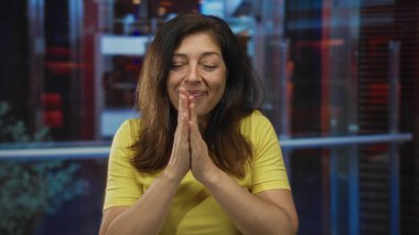 Sarı tişörtlü İspanyol orta yaşlı kadın otel odasındaki cam duvarlı çene yakınlarında avuç içlerini birbirine bastırıyor..