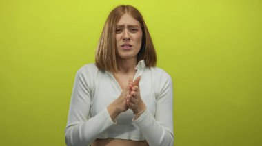 Sarışın genç bir kadın sarı bir stüdyoda kollarını göğsüne bastırıyor..