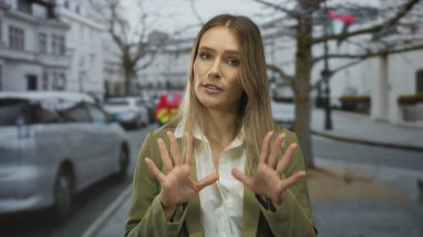 Kadın şehir sokaklarında sakin bir jest yapıyor. Arka planda arabalar ve binalar var. Açık hava ortamlarına olan güvenini gösteriyor..