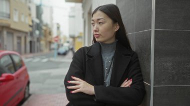 Şehir caddesinde kolları çapraz duran kadın şehir ortamında kendine güvenini ve tarzını gösteriyor..