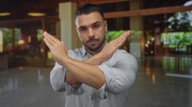 Otel binasının lobisinde çizgili gömlek giyerken kollarını kapalı tutan bir adam çevre ışığı altında reddediliyor..