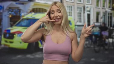 Sarışın bir kadın başparmağıyla kulağına, parmaklarıyla ağzına telefon hareketi yapıyor..