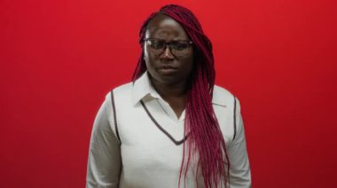 Kadın, elleri kulaklarında kırmızı duvara yaslanmış, canlı örgüler ve duygusal gösteriler sergiliyor..