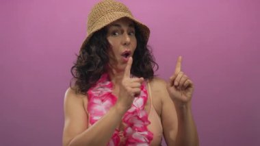 Orta yaşlı, bikini mayo giyen İspanyol bir kadın ve Hawaii zambağı fotoğraf stüdyosunda parmaklarını yan yana gösteriyor..