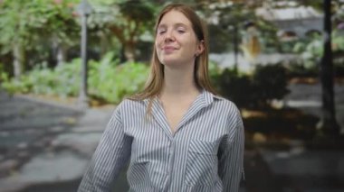 Yeşil bir gölgeliğin altında, yeşil bir gölgeliğin altında, yumuşak güneş ışığı ifadesine sahip sokak lambası direğinin altında, görünür yüzüyle gülümseyen genç bir kadın..