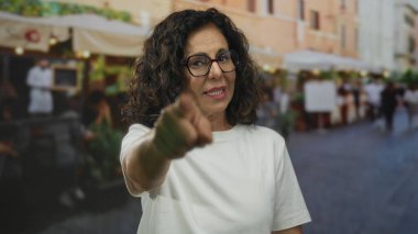 Hayat dolu bir sokak sahnesinde hareketli bir restoranın terasında kendine güveni ve hoş bir ifadeyle dikilen bir kadın..