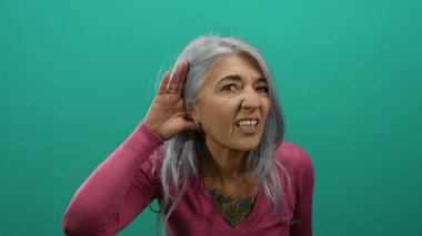 Pembe kazaklı, yeşil arka planda dinleyen yaşlı bir kadın, izole edilmiş bir duvarda düşünceli bir ifade ve düşünceli davranışlar sergiliyor..