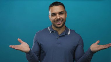 Polo tişörtlü genç adam gülümsüyor ve açık avuçlu jestler gösteriyor..