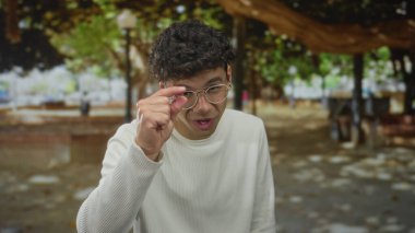 Genç İspanyol adam gülümseyen parmaklarını çimdikler güneş ışığında yeşil park; ince ince ince detay oyun.