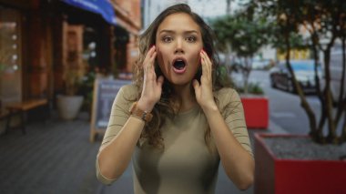 Canlı bir sokakta duygularını ifade eden bir kadın açık şehir ortamında şaşkınlık, eğlence ve tefekkür sergiliyor..