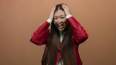 Kahverengi arka planda kırmızı ceketli bir kadın gülümsüyor, neşe ve güveni ifade ediyor..