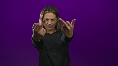 Mor bir stüdyoda orta parmak ve elleri gösteren bir kadın. Direk dik dik bakan, çatık kaşlı, meydan okuyan biri..