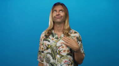 Stüdyoda göğsünde tropikal çiçekli gömlek ve omuzlarından dökülen uzun saçlı sarışın bir adam..