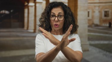 Orta yaşlı İspanyol kadın, eski şehir taş avlusunda inkar jesti olarak çıplak kollarını kavuşturuyor; reddediliyor..