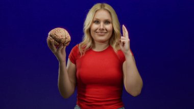 Umut dolu bir jestle beyni çapraz parmaklarla tutan kadın, umut verici bir hareket olarak mavi arka planda duruyor. Düşünce süreci ve zihinsel odaklanma gösteriyor..