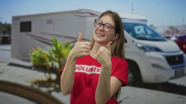 Kırmızı gömlekli genç sarışın gönüllü kadın güneşli şehir caddesinde çifte onay veriyor. Onaylandı..