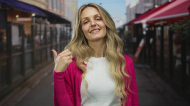 Restoran terasında gülümseyen pembe süveter giyen bir kadın şehir sokağında sarı saçlı, güpegündüz gideceği yeri gösteren bir el gösteren bir kadın..