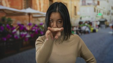 Kalabalık bir şehir caddesinde, açık bir restoran terasında el kol hareketi yapan Çinli genç bir kadın..