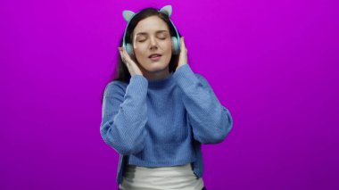 Renkli kulaklıklarla müzikten hoşlanan bir kadın canlı pembe arka plana karşı keyfi ve rahatlığı gündelik bir şekilde ifade ediyor..