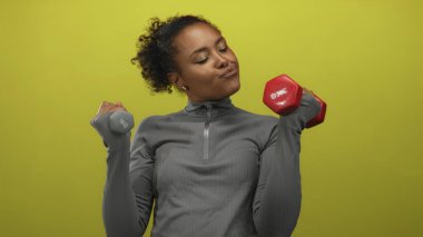 Atletik kadın yeşil stüdyoda bir çift kırmızı ve gri dambılı kaldırır ve gülümser..