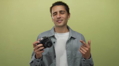 İzole edilmiş sarı arka plan duvarının önünde kamerayı tutan genç İspanyol bir adam kendine güvenen pozuyla fotoğrafçılığa ve yaratıcı ifadeye olan ilgisini gösteriyor..