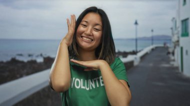 Genç Çinli bir kadın kumsaldaki bir deniz kenarında el kol hareketleriyle mutlu mesut dolaşır..