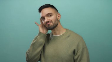 Zeytinli genç adam dikkatle dinliyor mavi arka plan karşısında merak ve dikkat gösteriyor