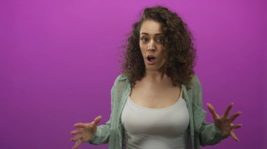 Elleri havada ve açık göğüslü bir kadın, mor atölyede beyaz kolsuz bluz giyiyor. Hayal kırıklığı hassasiyeti var..