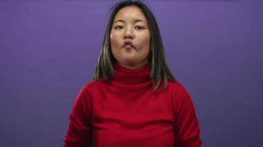 Mor arka planda kırmızı süveter giyen bir kadın, izole edilmiş bir stüdyoda mizah ve ifade gösteriyor..