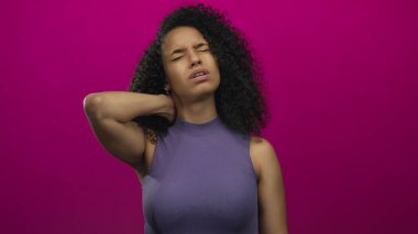 Boyun ağrısından muzdarip bir kadın canlı pembe bir arka planın önünde duruyor ve bir rahatsızlık ve gerilim anı yakalıyor..