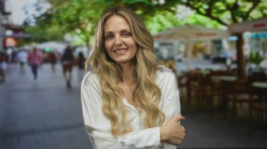 Zarif bir kadın bir restoranın içinde dudaklarını şişirirken genç sarışın bir kadın da sokağa bakan bir terasta durup gülümseyerek selamlıyor..