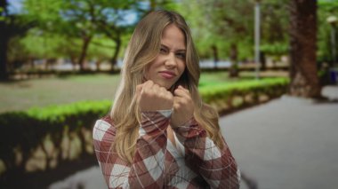 Kadın, sarı saçlı, yeşil güneşli parkta çıplak yumruğunu öne doğru sallıyor..