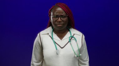 Steteskoplu ve örgülü bir kadın, profesyonel sağlık hizmeti teması taşıyan izole edilmiş mavi arka plana karşı duruyor