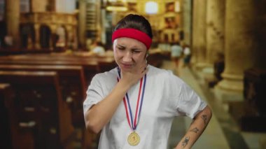 Madalya takan ve saç bandı takan kadın kilise ortamında derin derin düşünüyor. Antik mimari arasında spor ve ruhaniliğin bir karışımını sergiliyor..