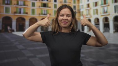 Güneşli bir plazanın yanında kameraya gülümseyen, kendine güveni onaylayan bir kadın..