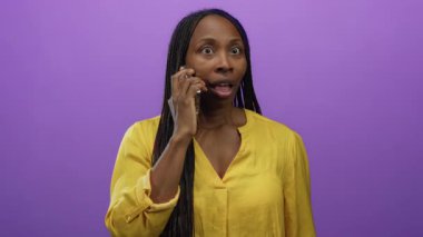 Akıllı telefondan konuşan, şaşırdığını ifade eden, sarı gömlek giyen, mor arka planda izole edilmiş neşeli iletişim ve modern yaşam tarzı sergileyen bir kadın..