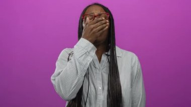 Örgülü ve gözlüklü bir kadın canlı pembe bir arka planda hapşırıyor, ağzını kapatıyor, soğuk bir hissi ifade ediyor..